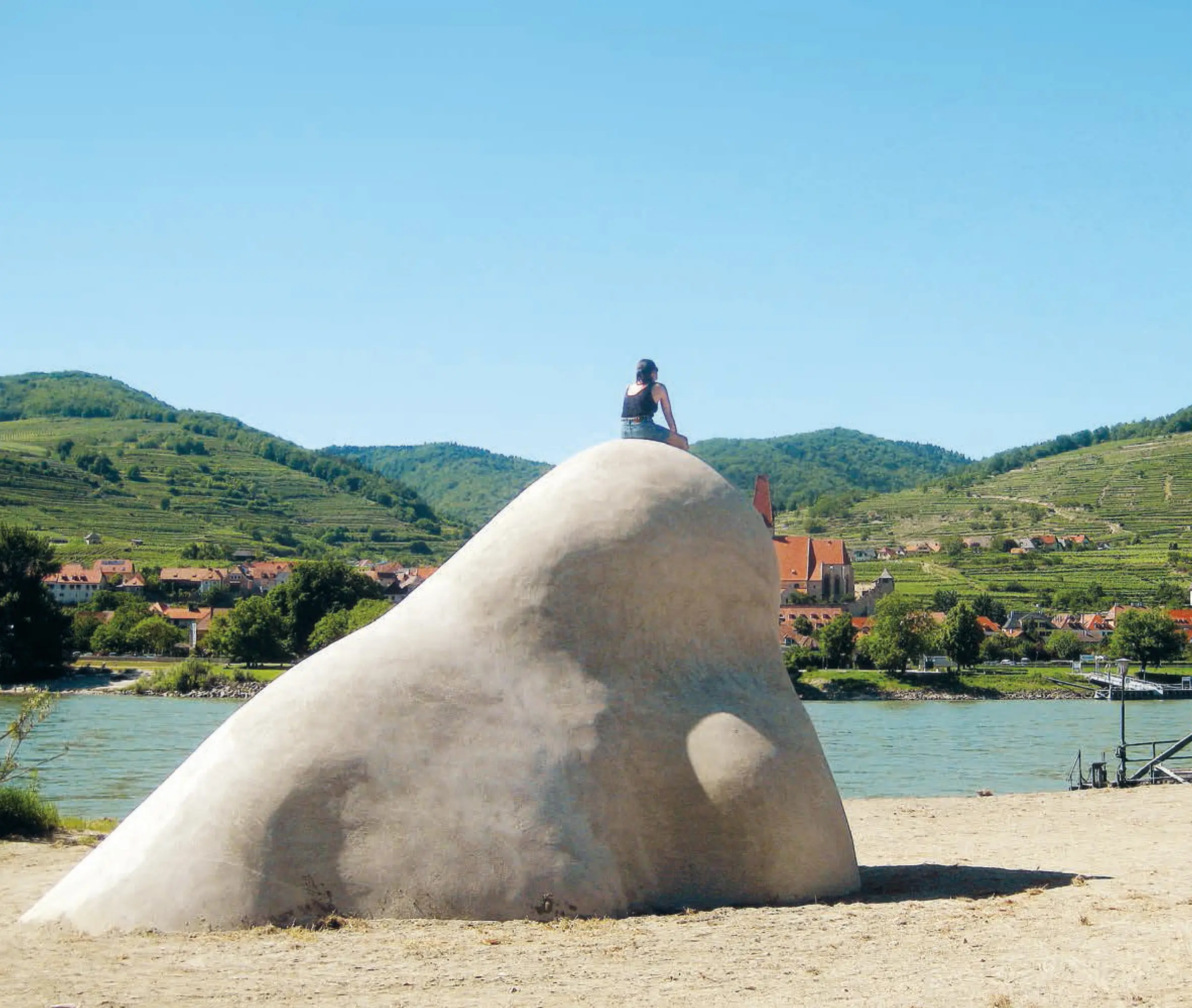 Frau sitzt auf Nasenspitze der Wachauer Betonnase und blickt in die Ferne zum Gegenufer (Wachau)